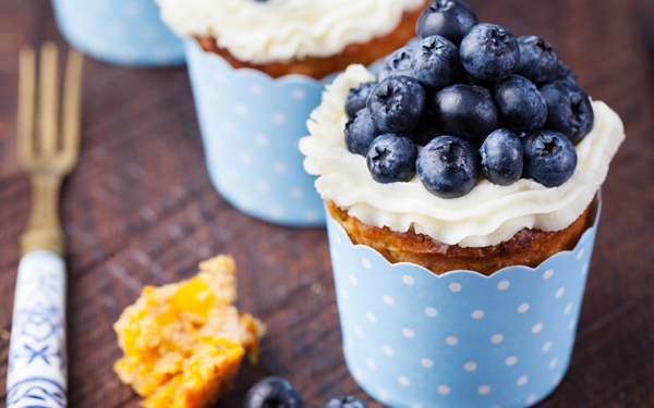 Estos cupcakes de calabaza con crema de queso y arándanos son a la vez dulces, especiados, frescos y aromáticos; ¡lo tienen todo! No te prives de disfrutar de la repostería otoñal durante todo el año. Sería una pena renunciar a unas magdalenas tan deliciosas. Paso 1: Precalienta el horno a 180ºC. Parte la calabaza en rodajas de un centímetro de grosor y repártelas en una bandeja de horno cubierta con papel sulfurizado. Mete la calabaza al horno durante unos 20 minutos o hasta que al pinchar con un cuchillo la notes blanda. Intenta que no se tueste. Paso 2: Saca la bandeja del horno (¡pero no lo apagues!) y deja enfriar las rodajas de calabaza. Cuando estén tibias, pásalas por la batidora o por el procesador de alimentos hasta reducirlas a una pasta. Paso 3: En un recipiente amplio, bate los huevos y el azúcar con las varillas hasta obtener una mezcla clarita y espumosa. Si quieres resultados más rápidos, utiliza en este paso unas varillas eléctricas. Paso 4: En otro recipiente, tamiza la harina, la levadura y el bicarbonato y échalos poco a poco en la mezcla de huevos y azúcar sin dejar de remover para que no queden grumos. Paso 5: Echa los huevos uno a uno y bate enérgicamente para integrarlos por completo antes de echar el siguiente. Paso 6: Agrega el puré de calabaza, la nuez moscada, la pimienta de Jamaica, la canela, el comino y la sal. Remueve muy bien hasta obtener una masa uniforme. Paso 7: Prepara las cápsulas de papel de los cupcakes metiéndolas en moldes de silicona o metal y disponiéndolos en una bandeja de horno. Vierte la masa en las cápsulas hasta llenarlas unos dos tercios de su capacidad. Cuando estén listas, mete la bandeja en el horno durante 20 minutos o hasta que al introducir una brocheta en la magdalena salga limpia. Paso 8: Mientras se hornean los cupcakes, prepara el frosting, es decir, la crema que los cubrirá. En un recipiente mezcla la mantequilla en pomada (mantequilla a temperatura ambiente y con textura cremosa) con la crema de queso, el azúcar glas y la esencia de vainilla hasta que quede una crema de color uniforme. Paso 9: Saca los cupcakes y déjalos enfriar sobre una rejilla. Cuando estén tibios, reparte la crema de queso por encima. Si quieres que resulte más elaborado, prepara una manga pastelera con boquilla rizada y mete la crema dentro. Lava y seca cuidadosamente los arándanos. Presentación: Sirve tus cupcakes con crema de queso y arándanos por encima sobre una tabla de madera. Acompáñalos de una infusión suave o un buen vaso de leche. Sugerencia: Para la crema que coronará tus cupcakes confía en el queso de untar DIA y la mantequilla DIA. Te proporcionarán una calidad y sabor insuperables.